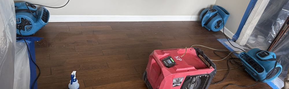 Dehumidifier and three air movers set on a hardwood floor inside poly containment