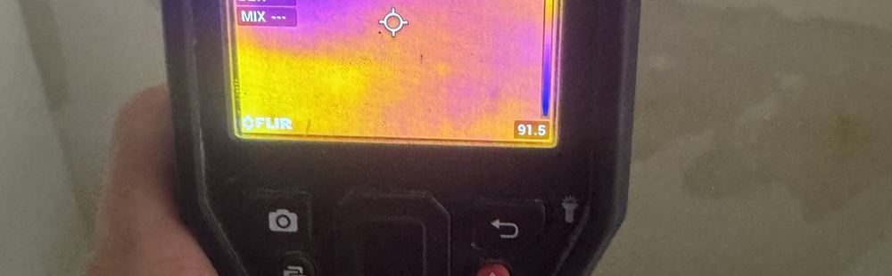 Thermal moisture meter held against a stained ceiling, wet area shown on screen