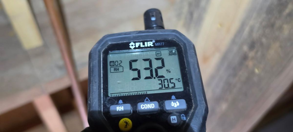 FLIR moisture meter in a gloved hand reading 53% relative humidity under a crawlspace floor