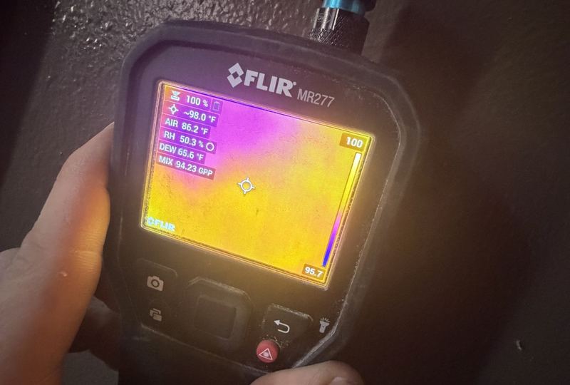 Thermal camera screen held in hand showing a wet area on a wall